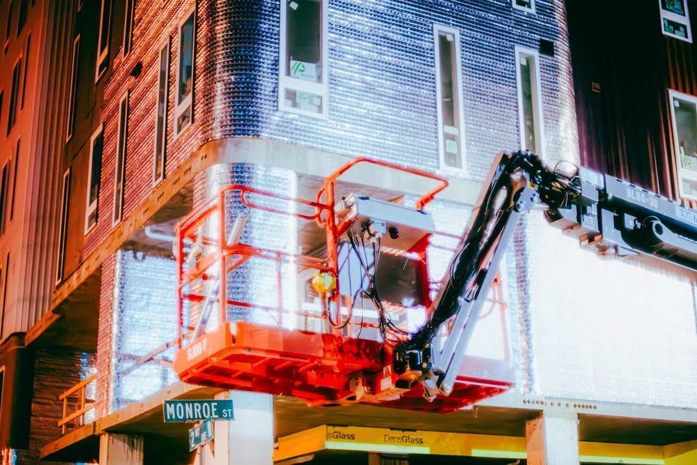 A vivid red lifting platform outside a brick building at night.