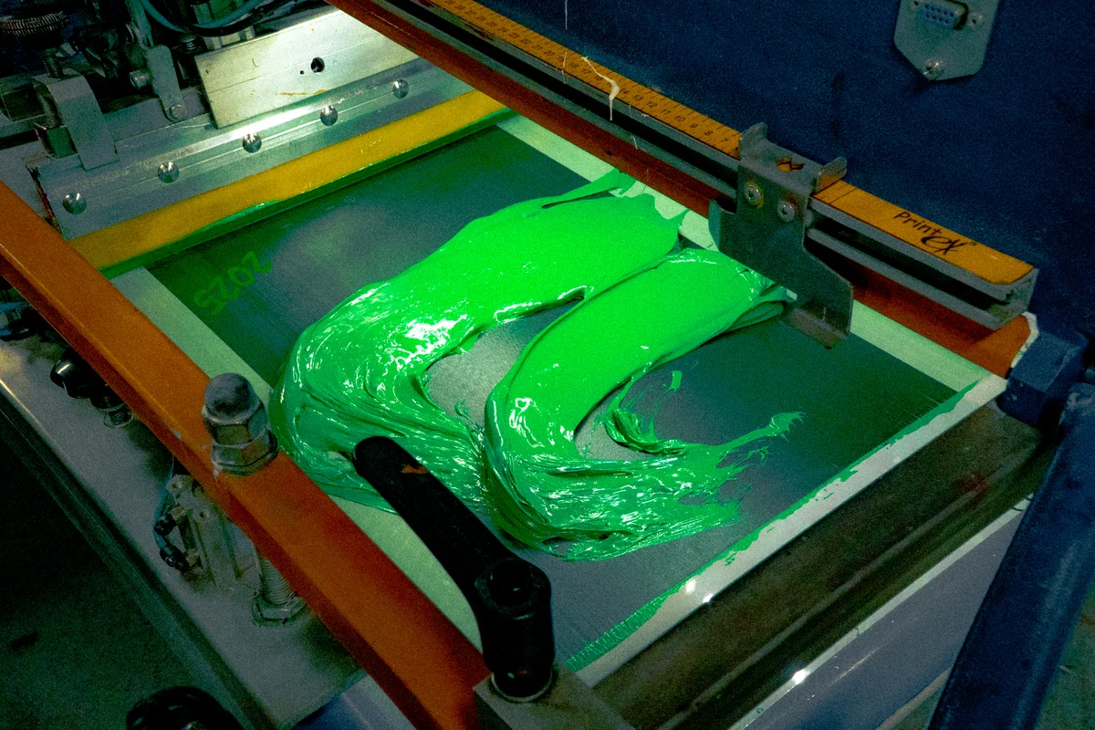 Vivid green ink across a screen-printing press.